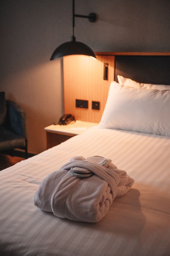 gallery-1 A cozy hotel room featuring a plush robe on the bed under warm lighting, epitomizing comfort and relaxation.