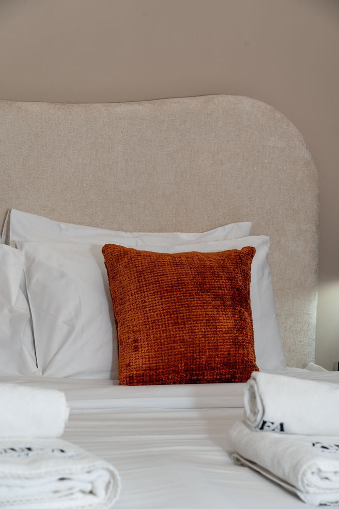 services-01 Elegant bed with vibrant orange cushion and fresh towels in a Dubai setting.