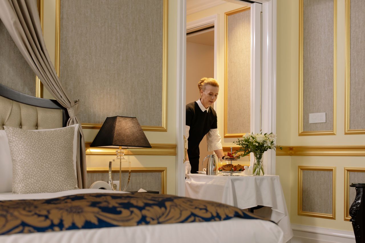 hero-img-02 A hotel employee delivers elegant room service with a tray of breakfast in a luxurious hotel setting.