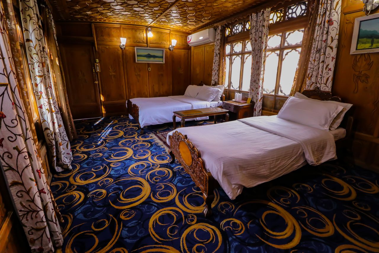 services-01 Elegant hotel room with wooden furnishings and twin beds, featuring artistic carpet and curtains for a cozy stay.